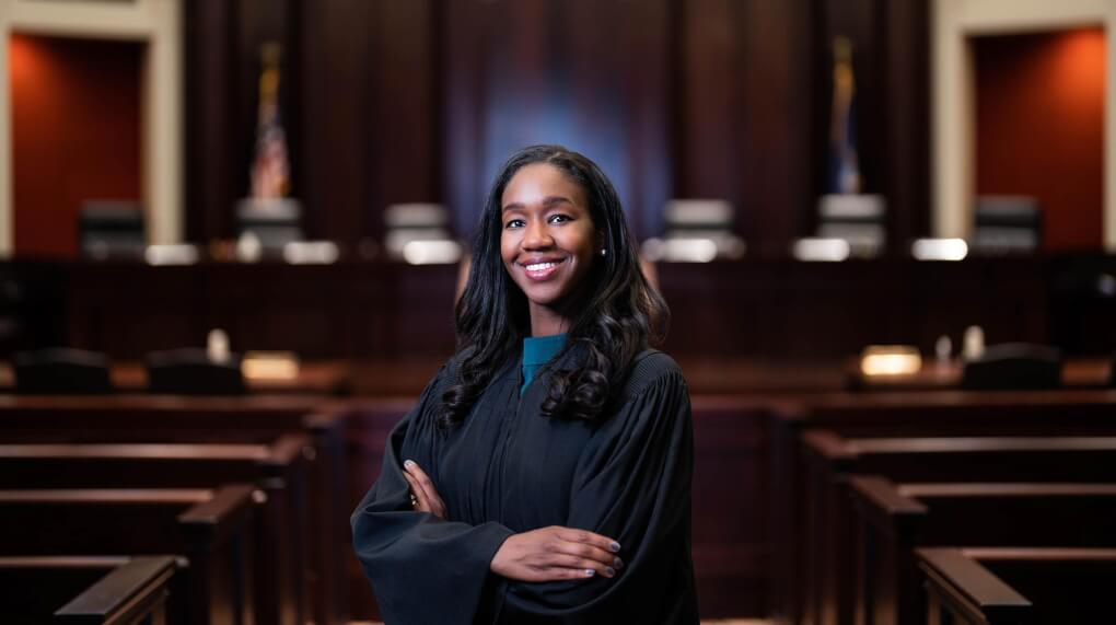 Justice Kyra Bolden stands in the court room wearing a black robe and crossing her arms and smiling